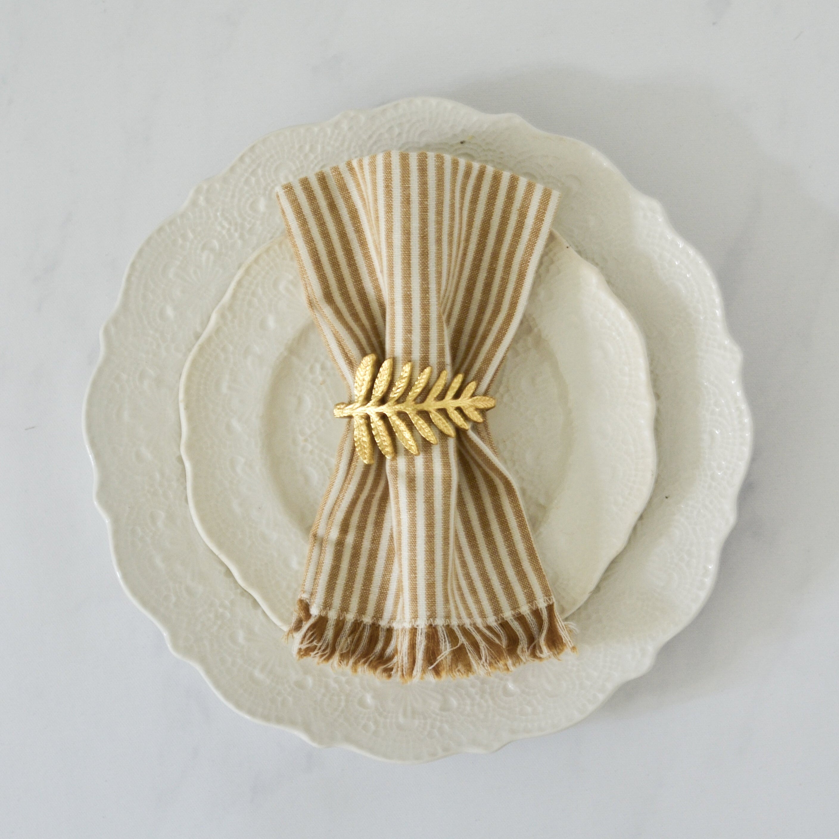 Napkin with a gold napkin ring on a white plate against a light gray background